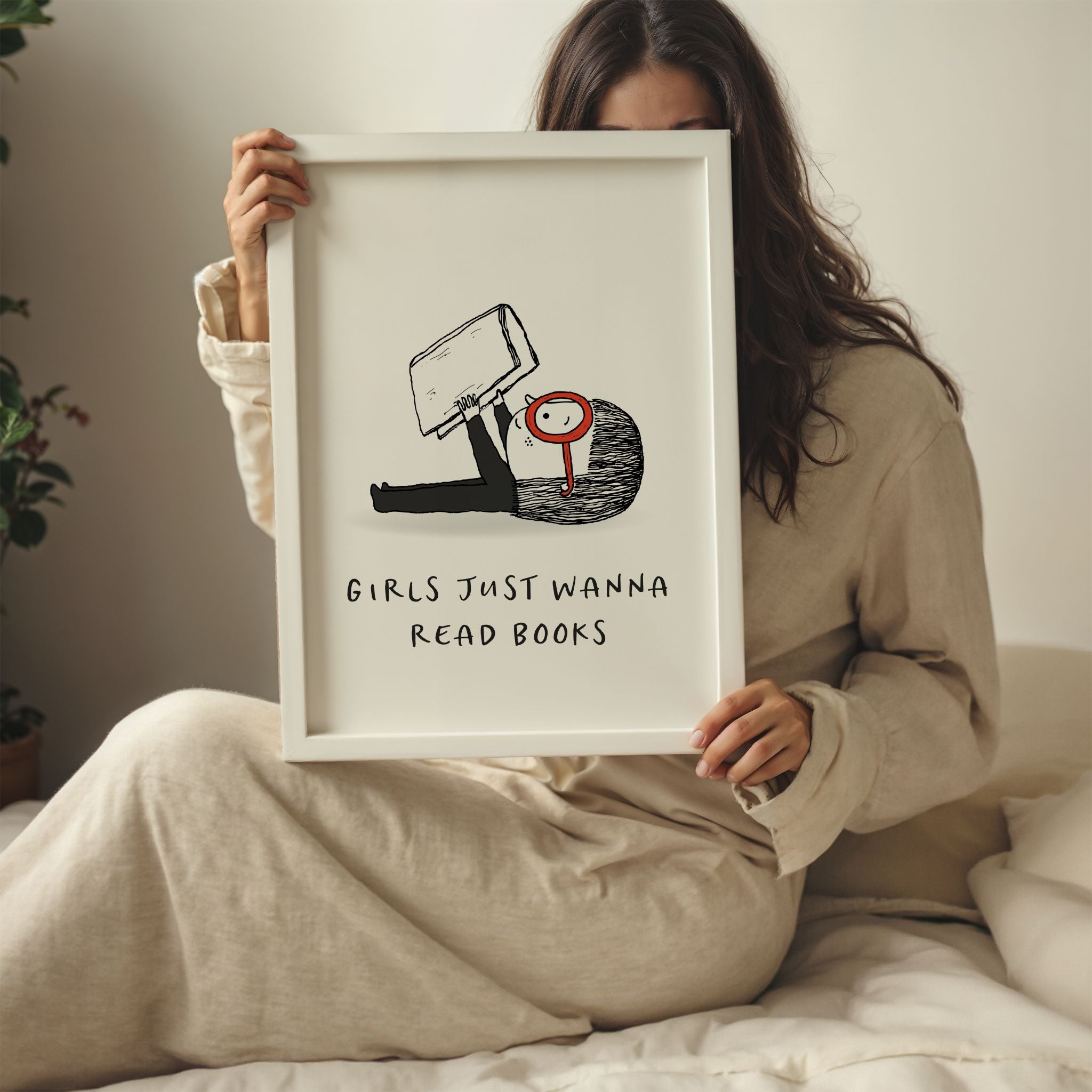 Woman sitting on a bed and holding a framed print with a cartoon character and text 'Girls just wanna read books'.