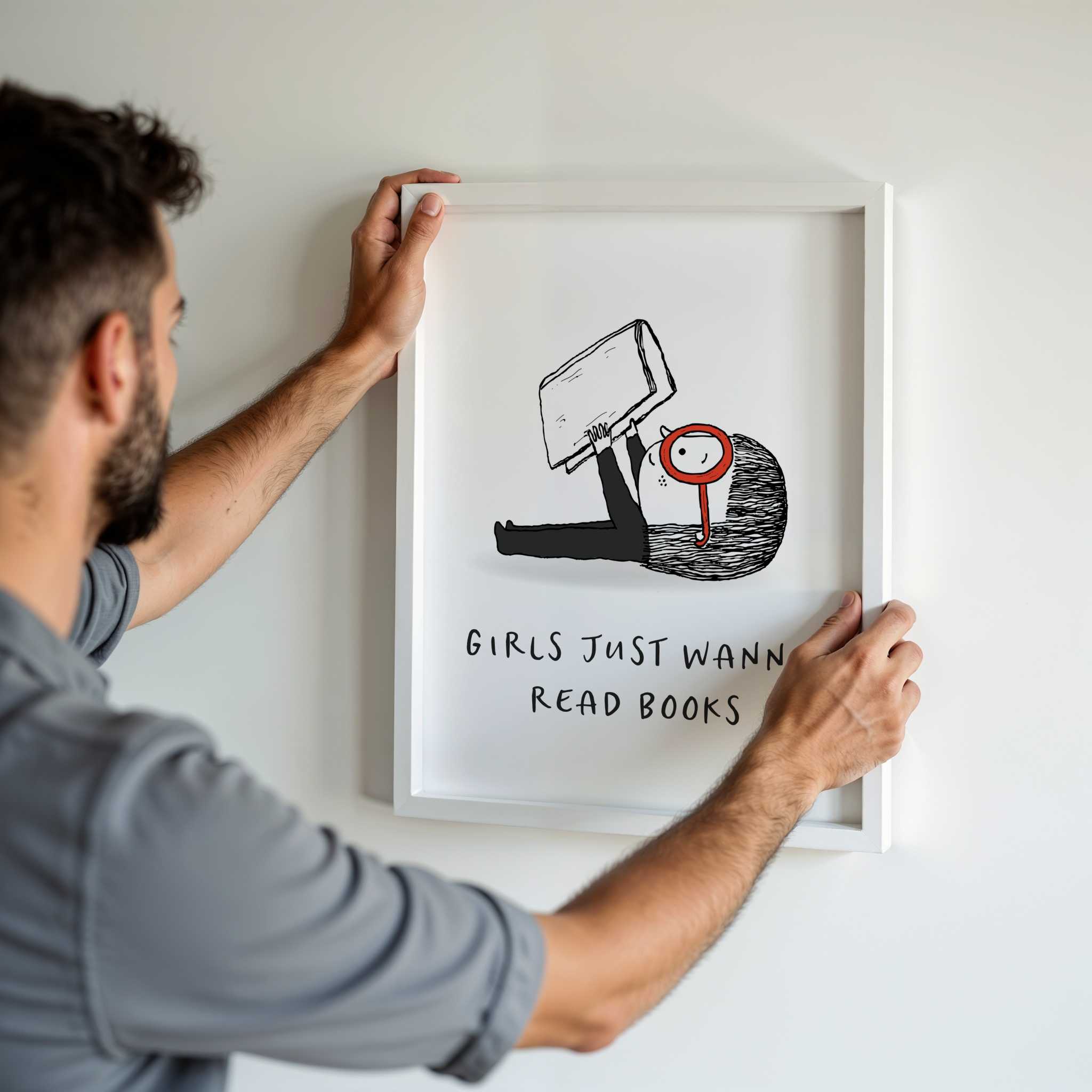Man hanging a framed illustration on a wall with text 'Girls Just Wanna Read Books'.