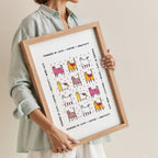 Woman holding a framed print with colorful cat illustrations and text.