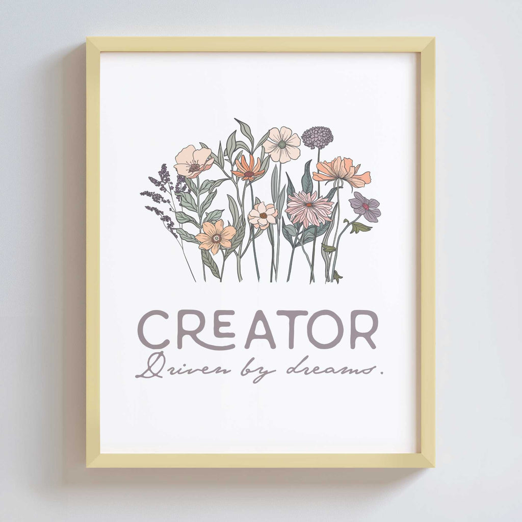 Artwork in a gold metal frame with floral design and text 'CREATOR Driven by dreams.' on a white background