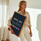 Woman holding a sign with 'Small Biz Big Heart' text in a bright room.