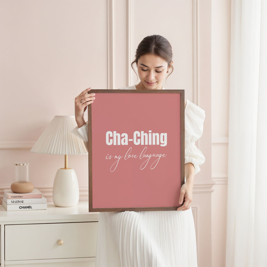 Woman holding a framed quote in a stylish room. Text says 'Cha-Ching is my love language.'