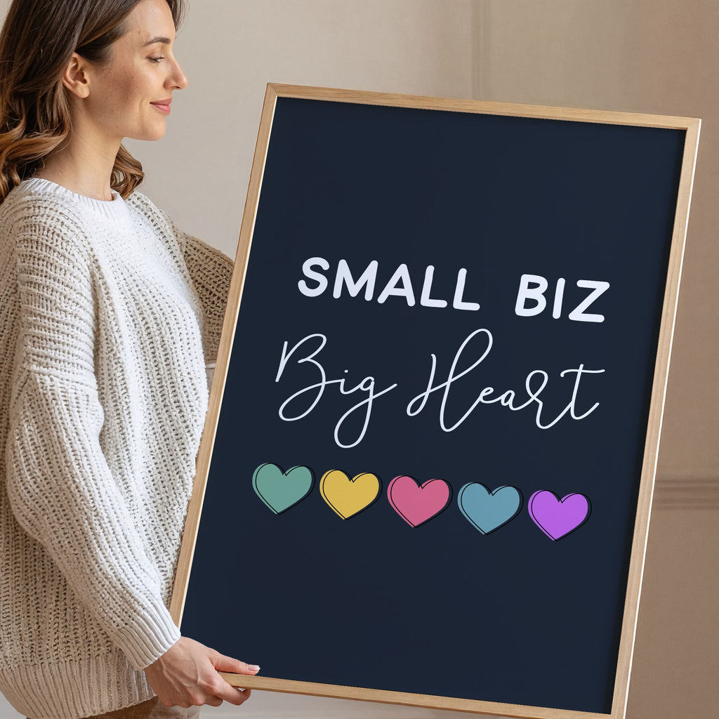 Woman holding a framed poster with 'Small Biz Big Heart' and colorful hearts.