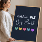 Woman holding a framed poster with 'Small Biz Big Heart' and colorful hearts.