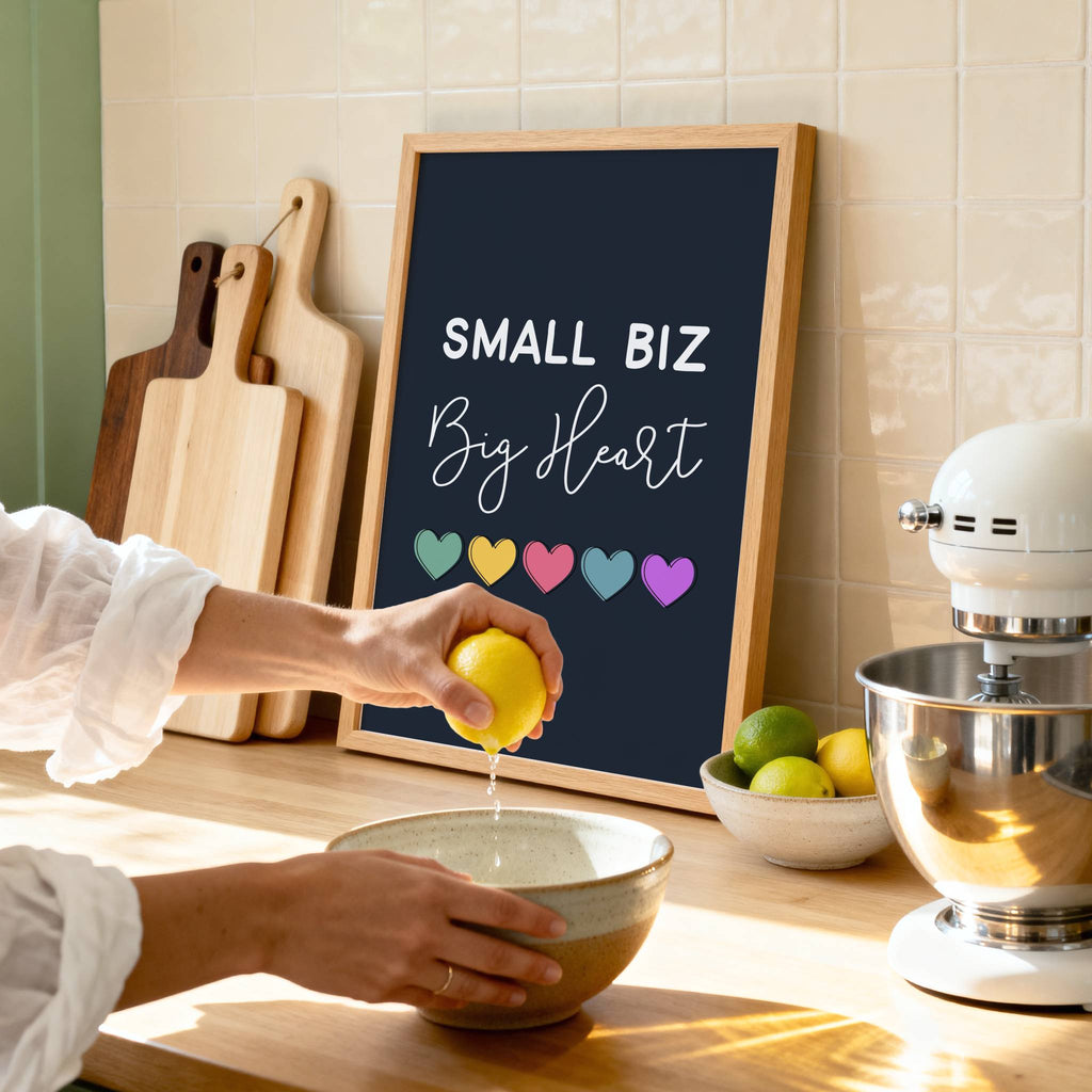 Person squeezing a lemon over a bowl in a kitchen with a 'Small Biz Big Heart' print in an oak frame.