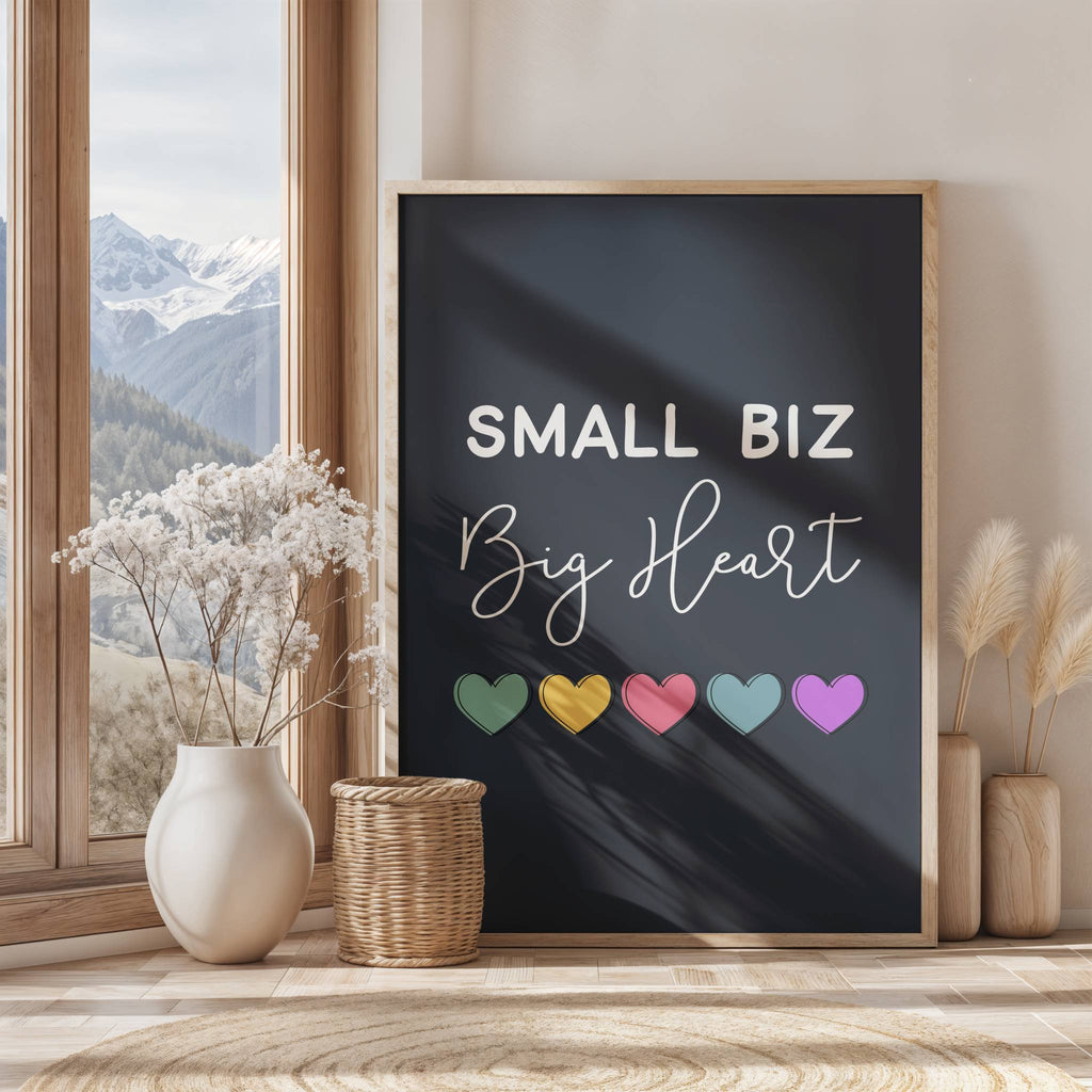 Framed poster with 'Small Biz Big Heart' text and colorful hearts on a wall with a window view of mountains.