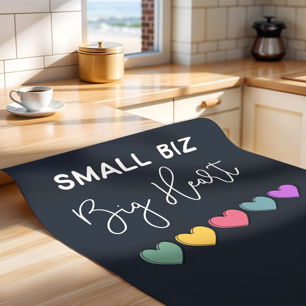 Unframed print with 'Small Biz Big Heart' text and colorful hearts on a wooden counter.